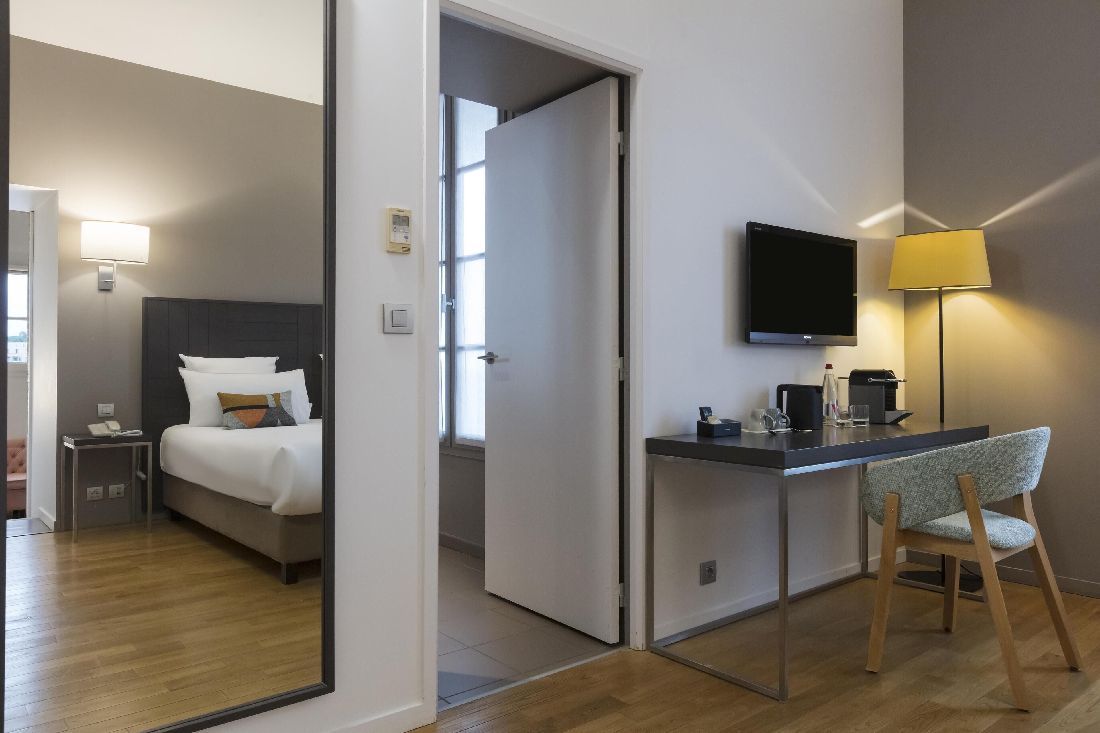 Une chambre d’hôtel comprenant un lit, un bureau avec une chaise, une télévision et une lampe.