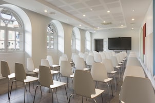 Un salón de conferencias con filas de sillas y una pantalla grande.