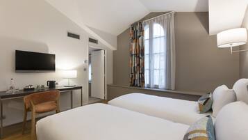 Una habitación de hotel con cama, escritorio con televisor, silla y ventana con cortinas.