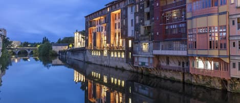 A riverside building with multiple balconies and a reflection in the water.