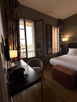 Una habitación de hotel con cama, un escritorio y silla, televisión y ventana con cortinas.