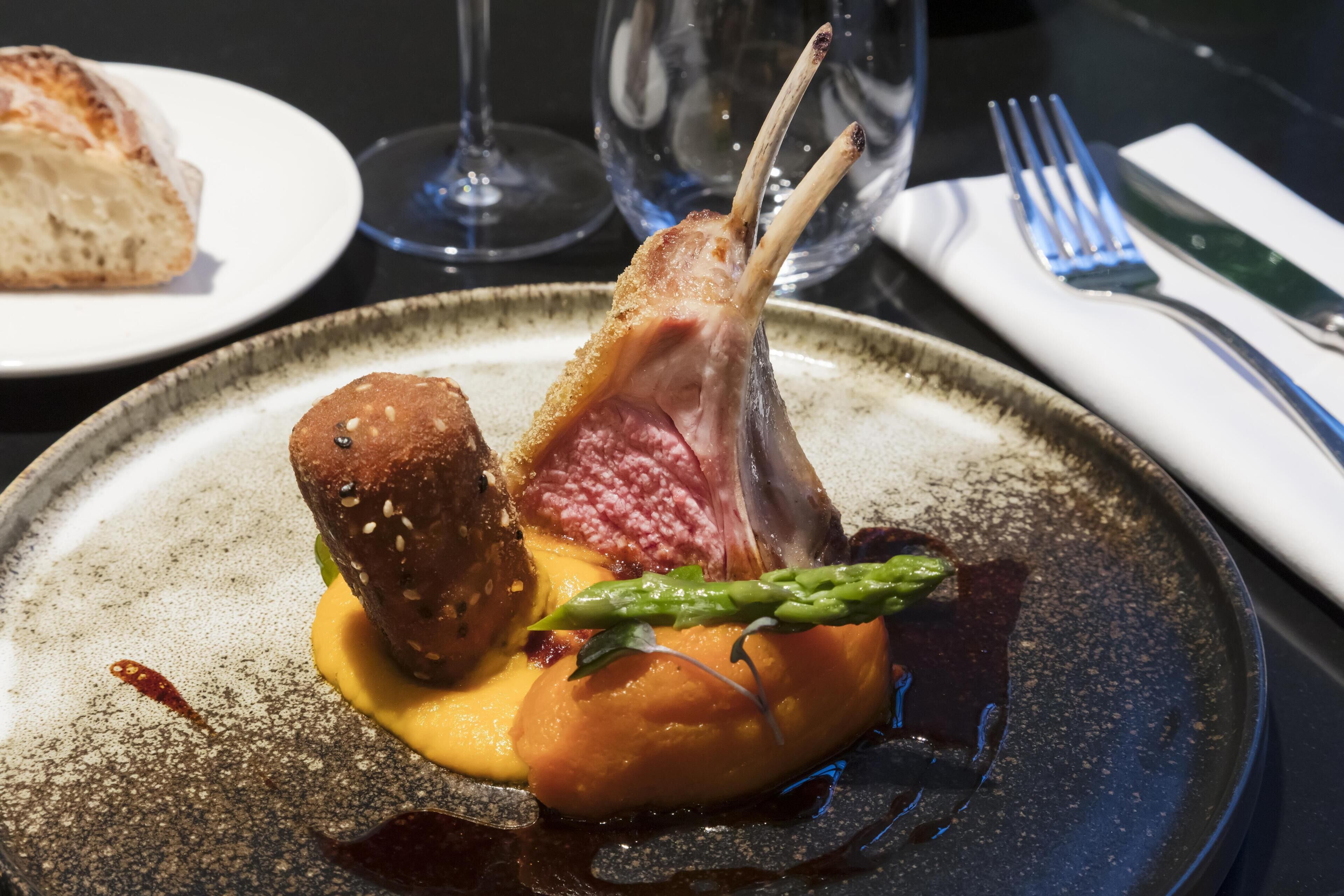 Une assiette avec une côte d’agneau, un morceau de pain et des asperges.