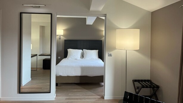 A hotel room with a bed, a bedside lamp, a chair, and a mirror reflecting the room. - Best Western Grand Hotel de Castres (Castres)