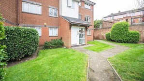 Un immeuble d’appartements en briques de deux étages, doté d’un petit jardin à l’avant, d’une porte de garage visible et d’une pelouse bien entretenue.