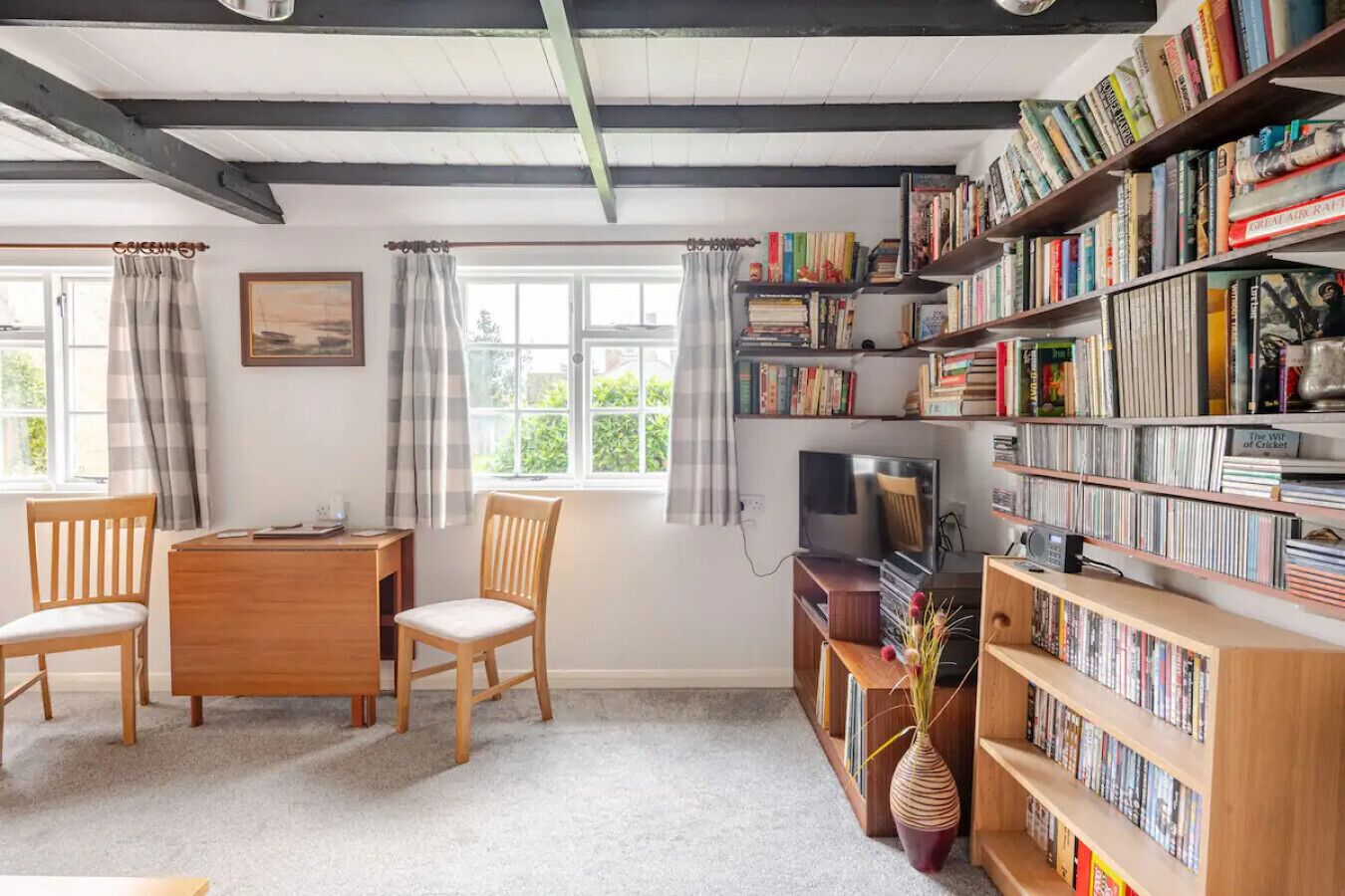 A cozy room with a wooden desk, two chairs, a television, and a bookshelf filled with books and DVDs.