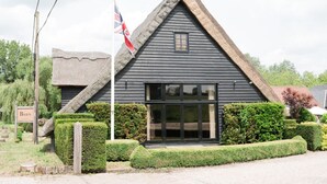A traditional building with a steeply pitched roof, a flagpole with a flag, and well-maintained hedges. - Cozy Cottage With Scenic Walks (Great Tey)