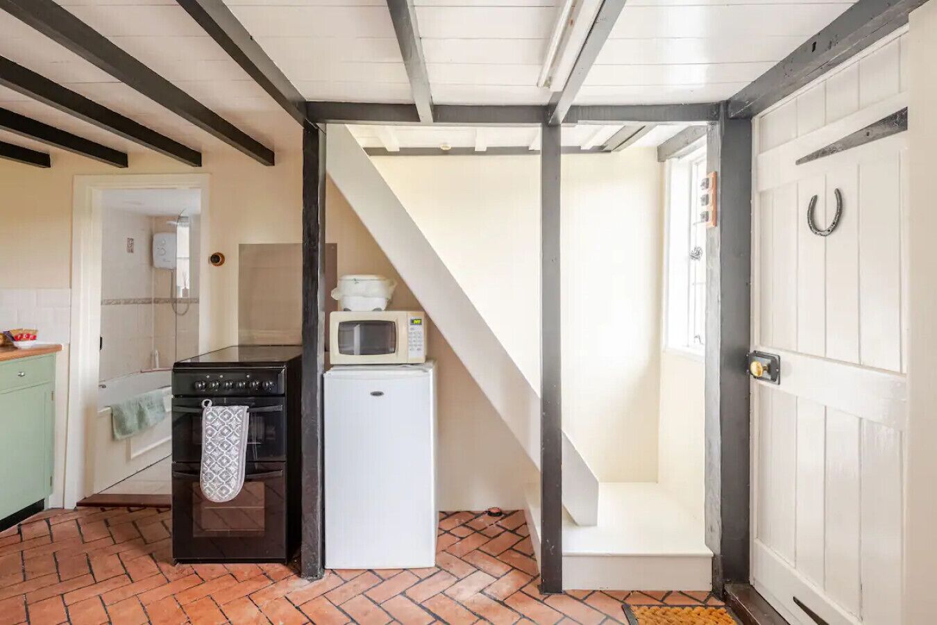 A compact kitchen with a stove, microwave, and refrigerator, a door with a horseshoe decoration, and a tiled floor.