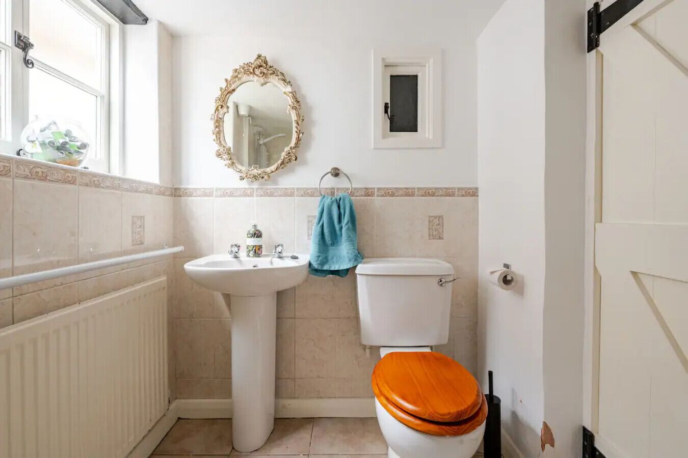 Une salle de bain avec un lavabo sur colonne, des toilettes avec un abattant en bois, un miroir décoratif et une serviette accrochée au mur.