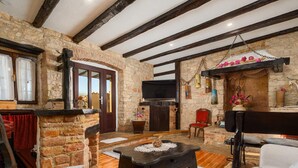 Un interior rústico con paredes de piedra vista, vigas de madera, chimenea y un televisor colocado encima.
