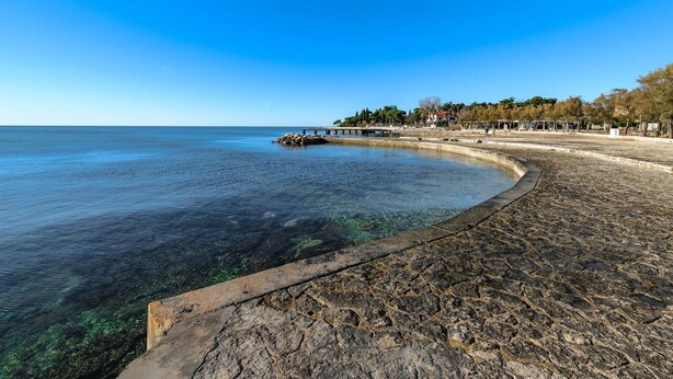 Una zona costera con cielo azul despejado, una playa arenosa y un litoral rocoso.