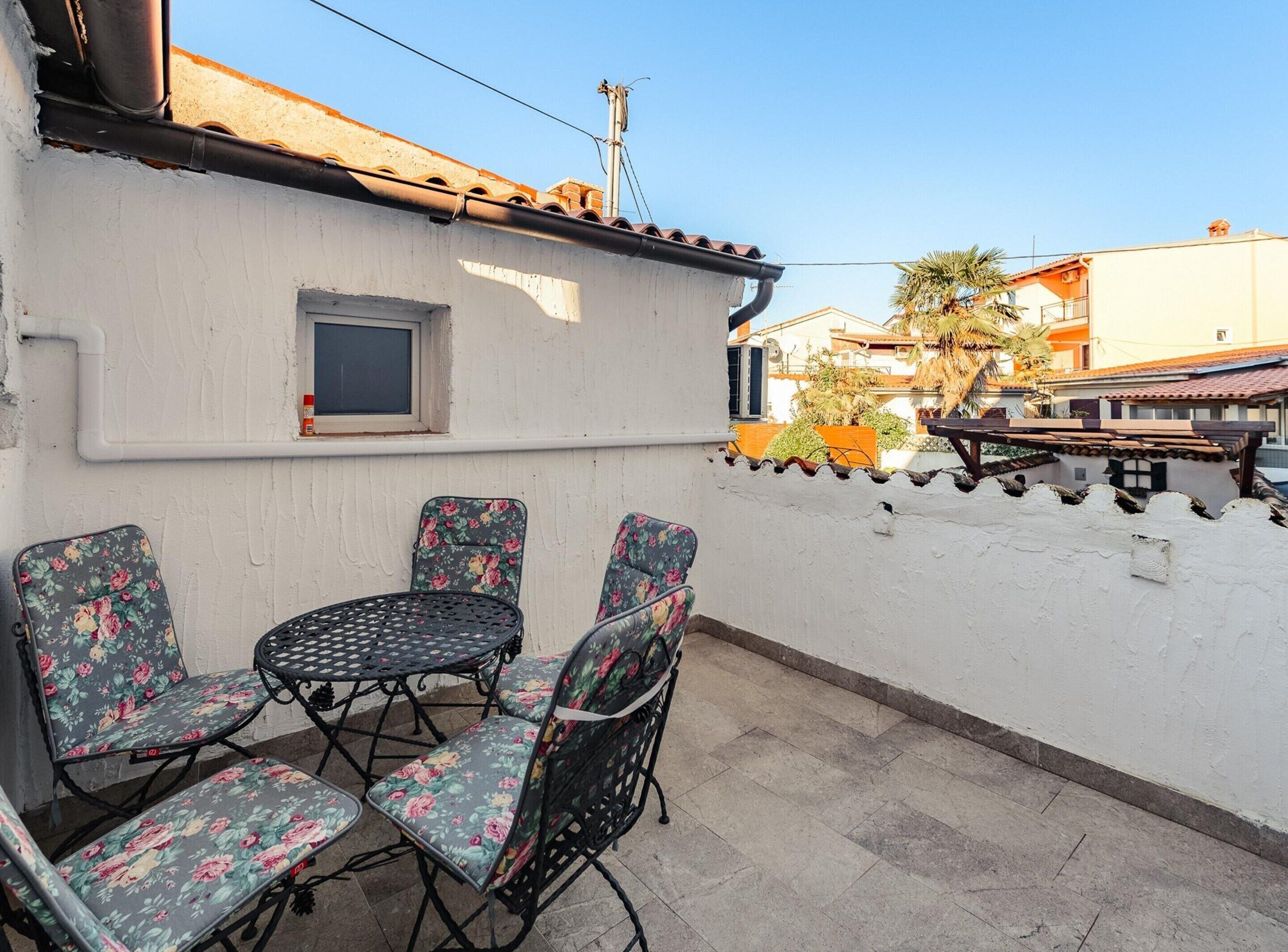 A patio with a table and four chairs, a small window, and a white wall.