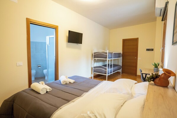 Une chambre d’hôtel avec un lit, une télévision, une porte en bois et une salle de bain visible à travers une porte ouverte.