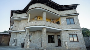 Ein mehrgeschossiges Gebäude mit einer Stein-Fassade, einem Balkon und zwei Statuen davor.