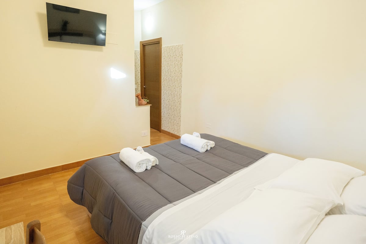 A hotel room with a bed, a flat-screen TV mounted on the wall, and a wooden floor.