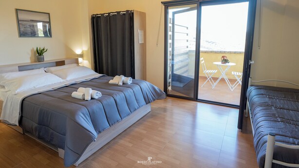 Ein Hotelzimmer mit Bett, kleinem Tisch mit Stühlen, einer Schiebetür zu einem Außenbereich und einem Blumentopf.