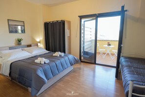 Une chambre d’hôtel avec un lit, une petite table avec des chaises, une porte-fenêtre coulissante donnant sur un espace extérieur et une plante en pot.