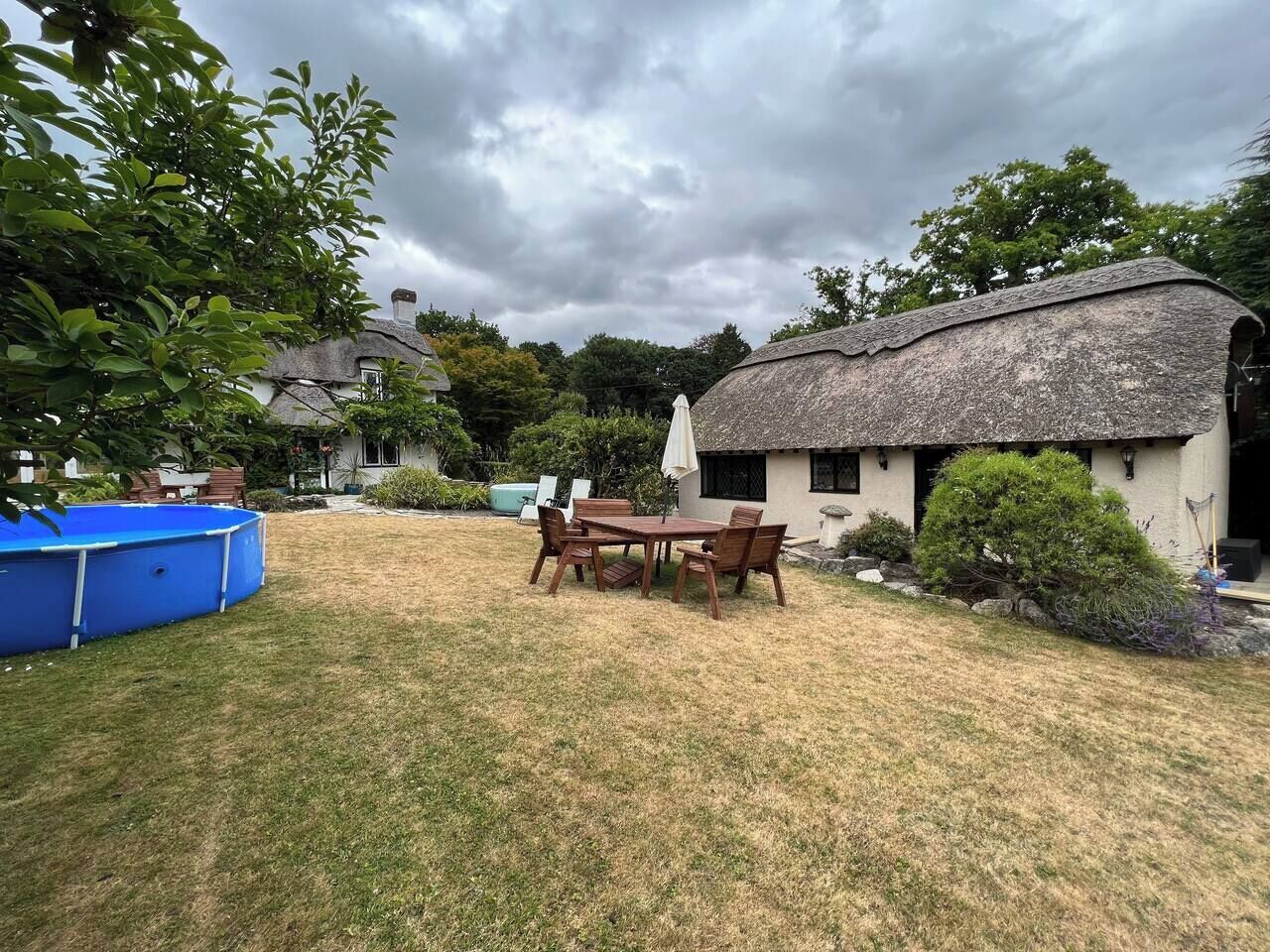 A backyard with a thatched-roof building, a wooden table with chairs, and a blue pool.