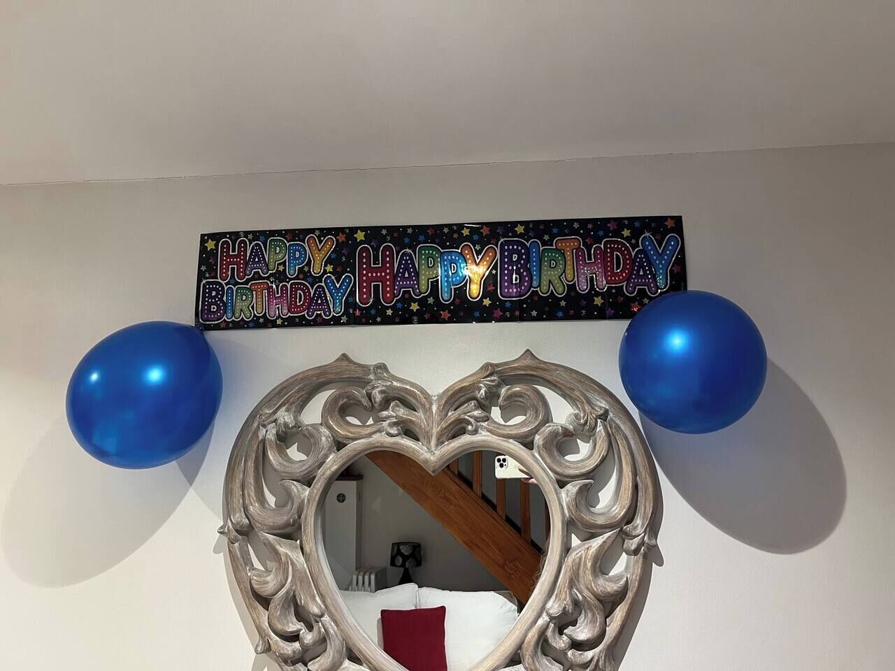 A room with a decorative mirror, a 'Happy Birthday' sign, and two blue balloons.