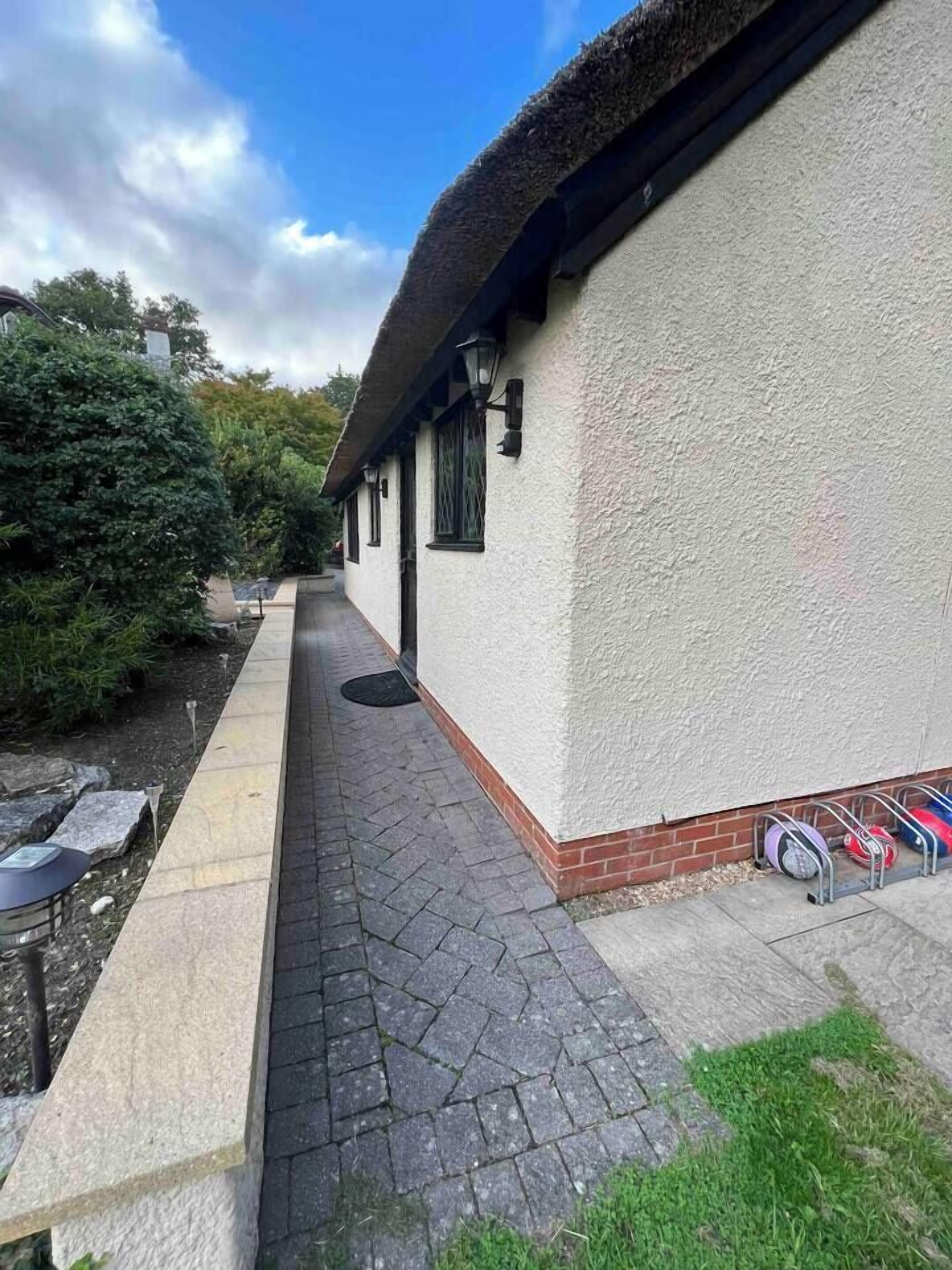 A narrow paved pathway leading to a building with a white exterior and a thatched roof. There are outdoor seating areas and a bike rack visible.