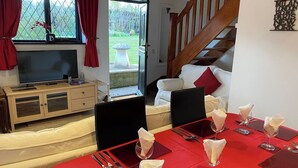 A dining area with a red table set for four, a wooden cabinet, a TV, and a staircase.