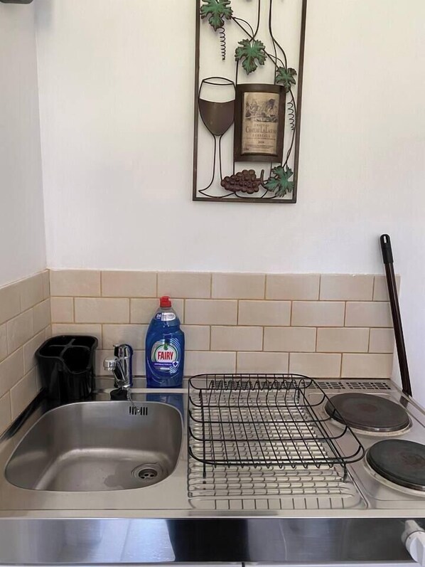 A kitchen with a stainless steel sink, a dish rack, a bottle of Fairy dish soap, and a decorative wall piece.