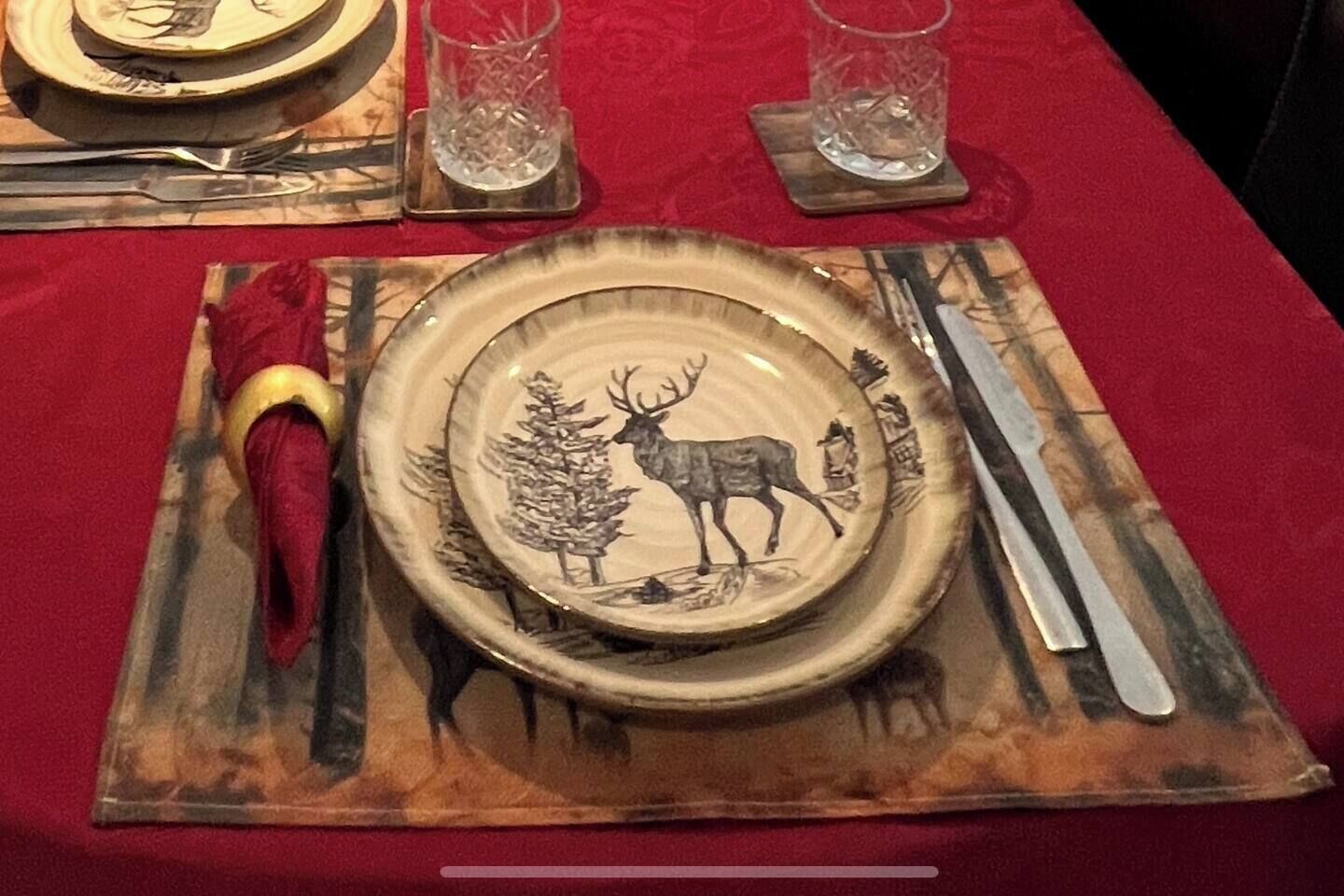 A table set with a plate featuring a deer and trees, a red napkin, and cutlery.