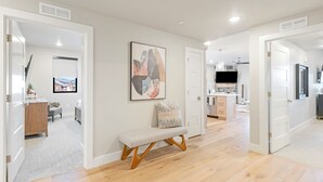 A spacious living area with a wooden bench, a colorful abstract painting, and a view of a mountain house through a window.