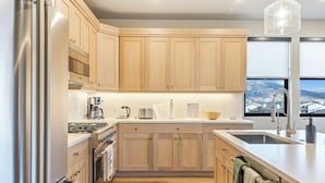 A modern kitchen with wooden cabinets, stainless steel appliances, and a view of a mountainous landscape through the window.