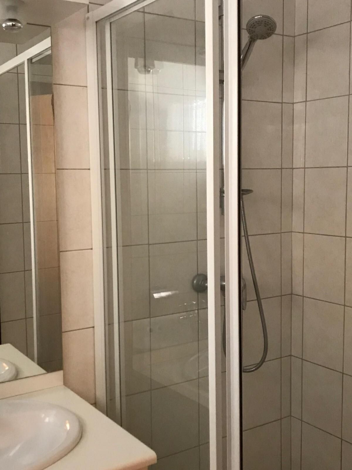Une salle de bain avec une douche à parois de verre, un lavabo blanc et un miroir.