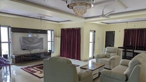Un salón amplio con un televisor de pantalla plana grande, asientos cómodos y una araña.