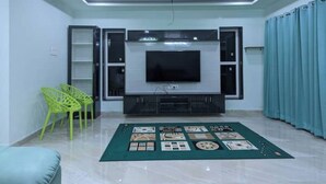 A modern living room with a flat-screen TV, a green chair, a patterned rug, and a blue curtain.