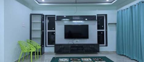 Una sala de estar moderna con un televisor de pantalla plana, un sillón verde, un tapete estampado y una cortina azul.