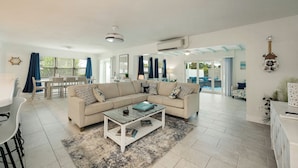 Un salón amplio con un sofá seccional color beige, una mesa de centro y una zona de comedor con una mesa y sillas blancas.