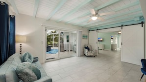 Amplia sala de estar con ventilador de techo, sofá con cojines estampados y vista a un patio exterior.