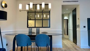 A modern dining area with a round table, two blue chairs, and a chandelier. - Alfred Suites is an elegant, upscale residence ideally located in the vibrant he (Dijon)
