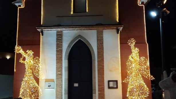 En kirke med et ur over indgangen, to oplyste statuer på hver side samt et kirketårn.