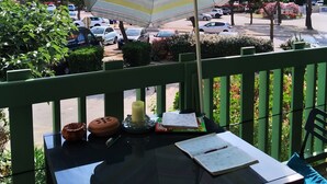En balkon med et bord, et mønstret parasol og udsigt til parkerede biler og bygninger.