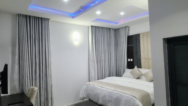 A modern hotel room with a large bed, grey curtains, a desk, and a chair.