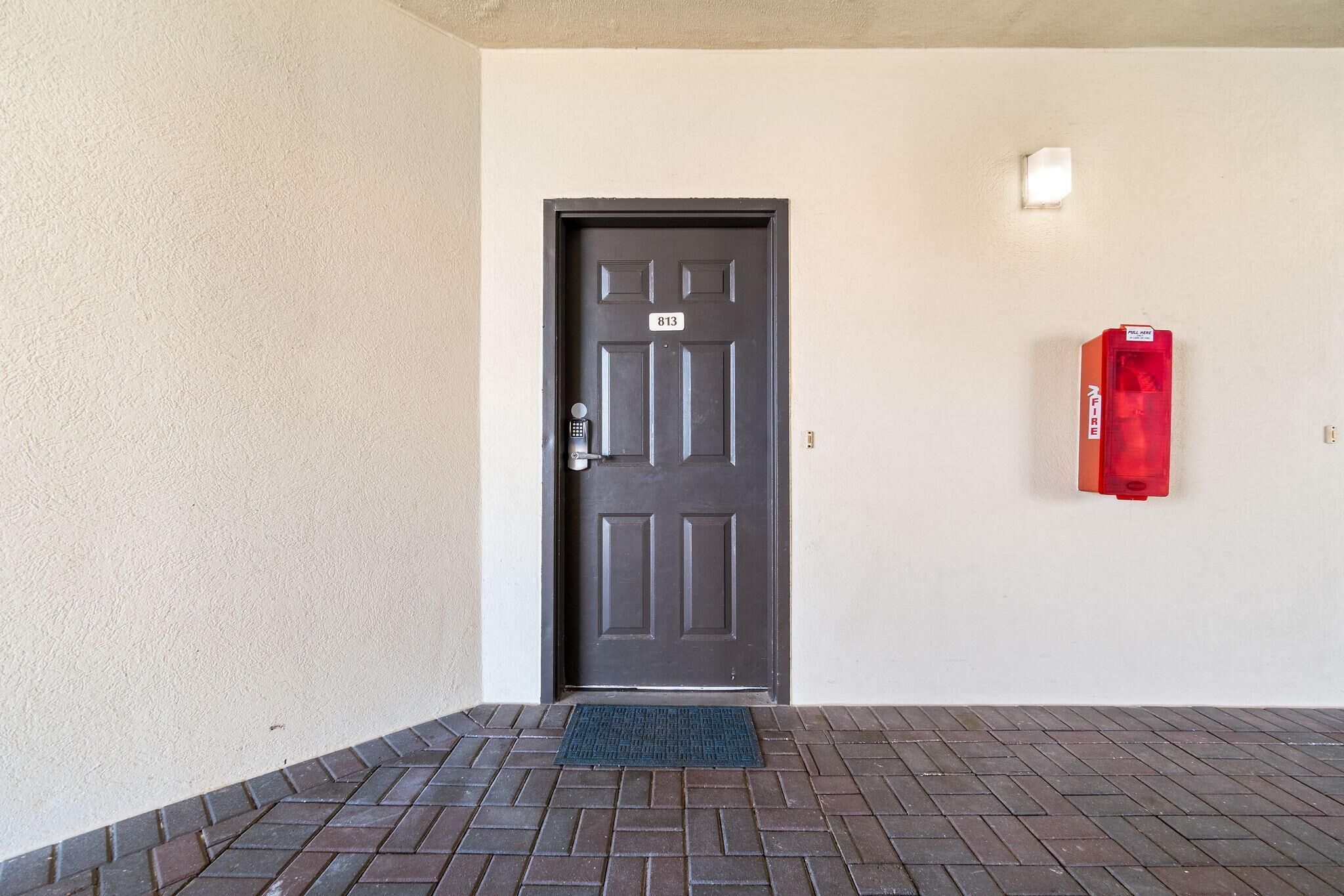 Una puerta con una placa de número, un extintor rojo y un felpudo.