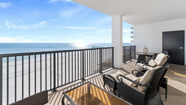 A balcony with a view of the beach, wicker furniture, and a black door. - The Palms West 813 (Orange Beach)