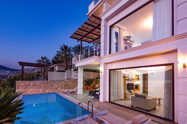 Una moderna casa a due piani con piscina, area salotto esterna e vista sulla città.