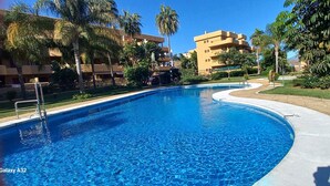 Una piscina a forma curva, circondata da palme e un edificio con numerosi balconi.