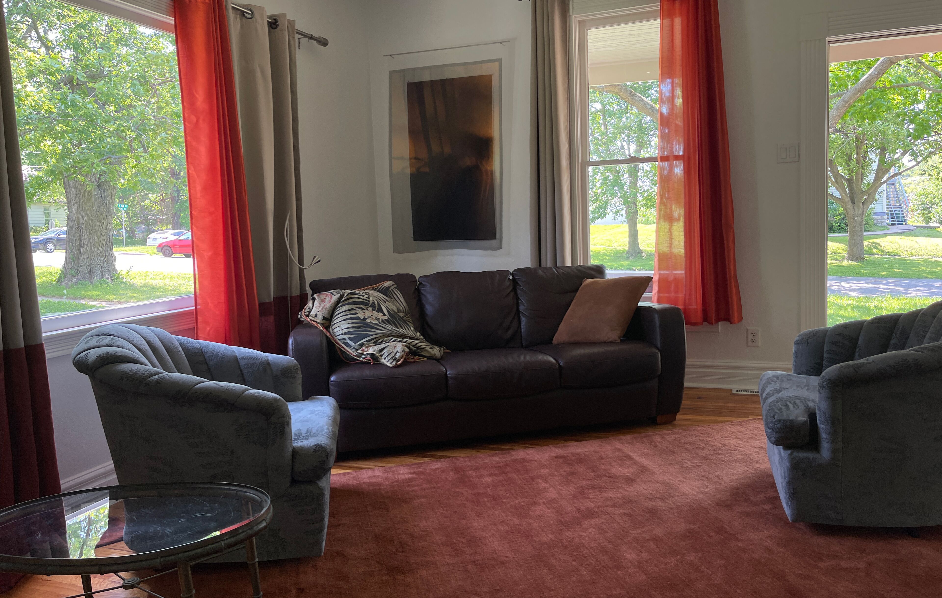 A living room with a dark brown sofa, two grey armchairs, and a glass coffee table.