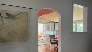 Een hal met een houten vloer, een witte muur met een kunstwerk en een raam met uitzicht op een buitenruimte.