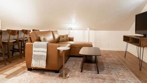 A cozy living room with a brown leather sofa, a small round table, and a television on a wooden stand. - The Loft at Park Place Cozy Studio on the Park (Columbus)