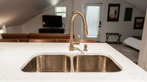 A kitchen with a large island, stainless steel sink, and a gold faucet. - The Loft at Park Place Cozy Studio on the Park (Columbus)