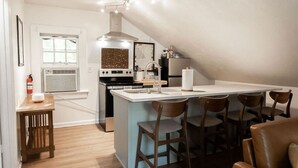 A modern kitchen with a central island, bar stools, and a dining area. - The Loft at Park Place Cozy Studio on the Park (Columbus)