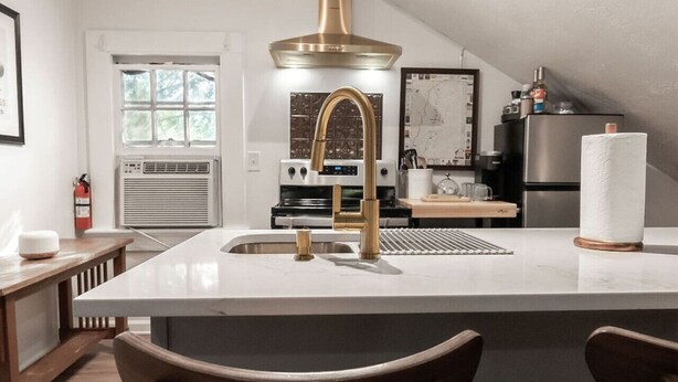 A modern kitchen with a central island, stainless steel appliances, and a large window. - The Loft at Park Place Cozy Studio on the Park (Columbus)