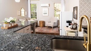 Una cocina con encimeras de granito, un fregadero, una cafetera y una zona de comedor con un sofá y sillas.