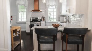 A modern kitchen with white cabinetry, a central island, and two black leather chairs. - Historic Park Place Retreat  3 Bdrm on the Park (Columbus)